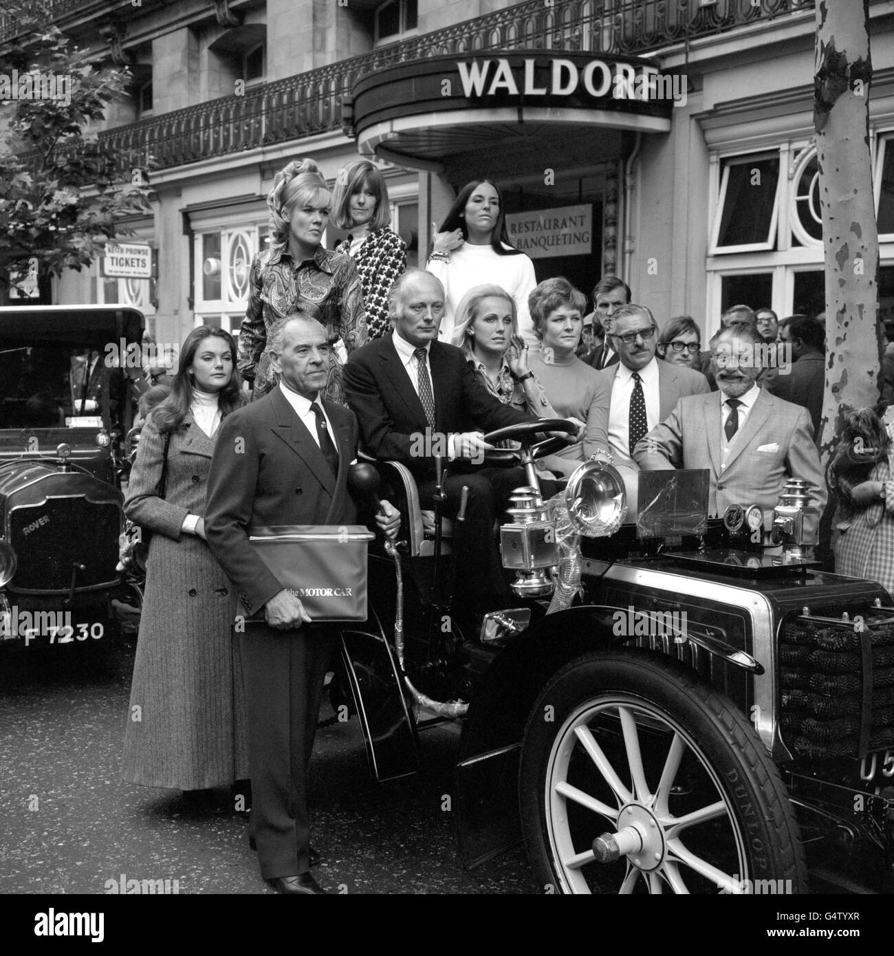 Lord Montagu of Beaulieu, at the wheel of a 1903 Gladiator, one of the veteran cars driven to the Waldorf Hotel, Aldwych, London for a reception to mark the publication of The History of the Motor Car. Standing beside him is Mr G Grampini, who was in 1928 a driver in the Alfa Romeo racing team at Brooklands. Passengers are some of the women motoring personalities who attended the reception. Stock Photo