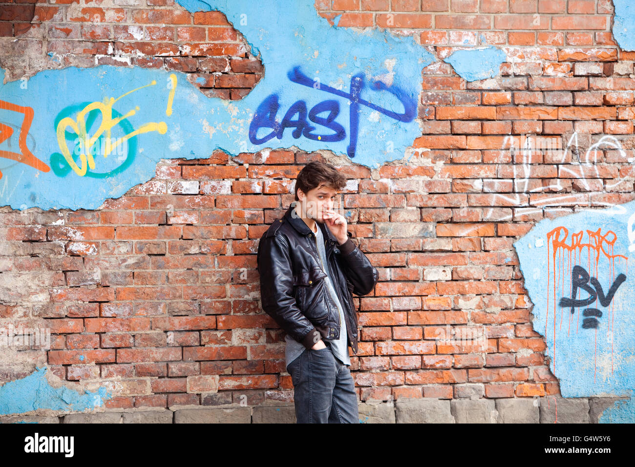 Young Man Standing by Brick Wall Looking Stock Photo