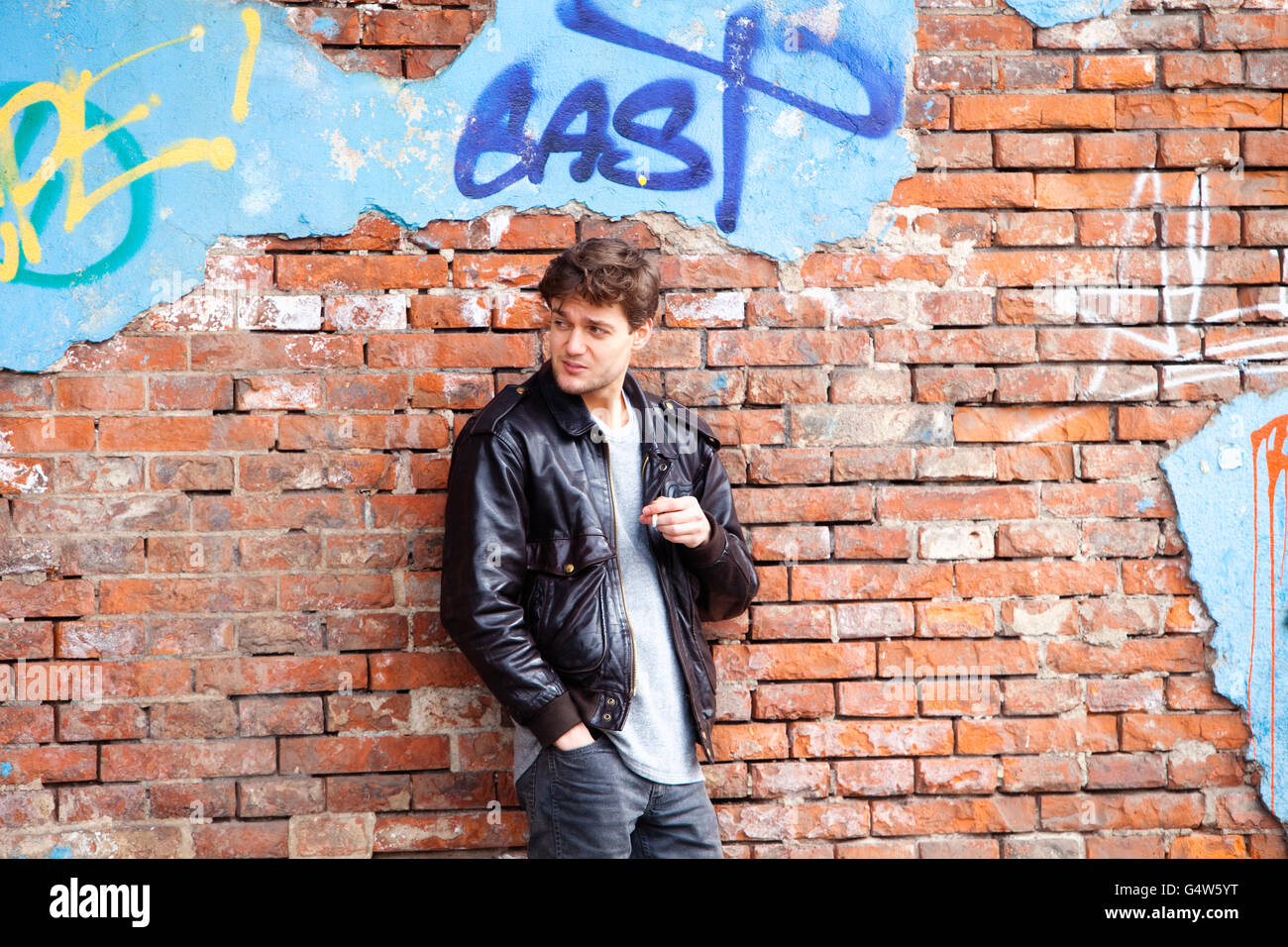 Young Man Standing by Brick Wall Looking Stock Photo