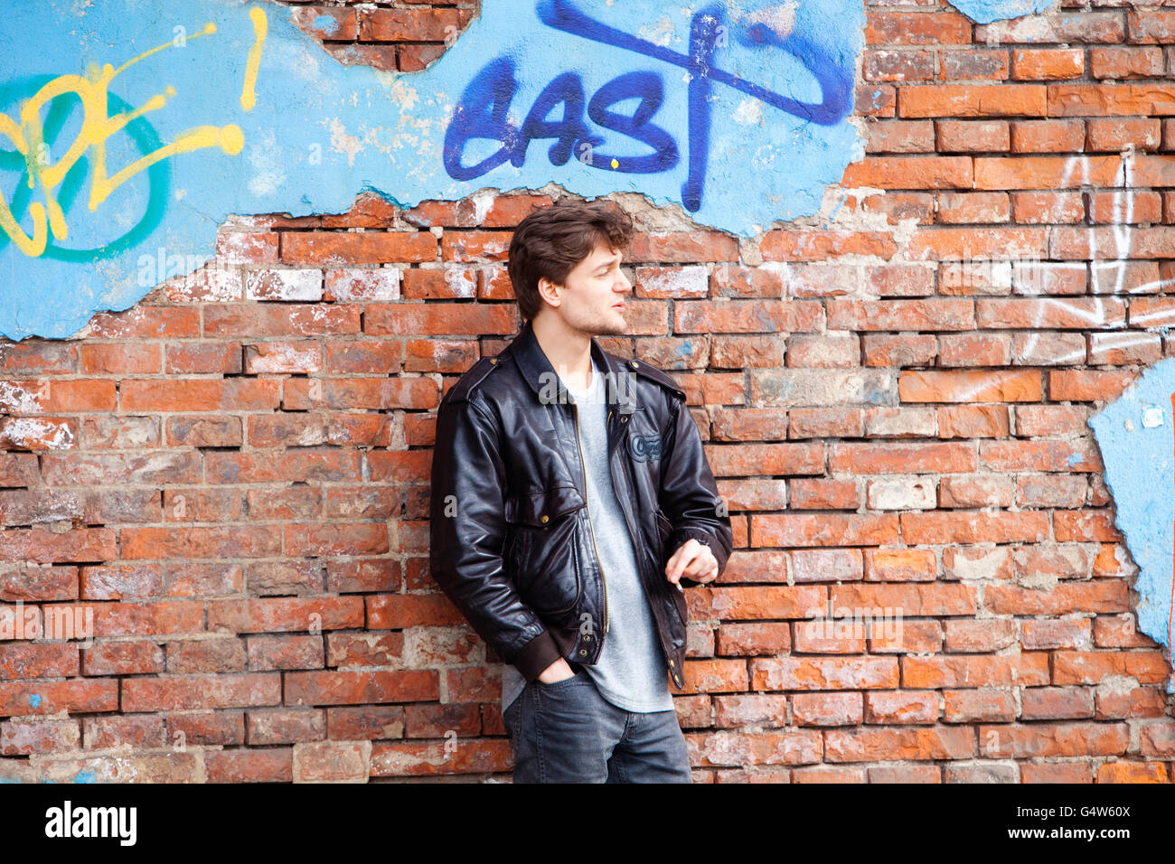 Young Man Standing by Brick Wall Looking Stock Photo