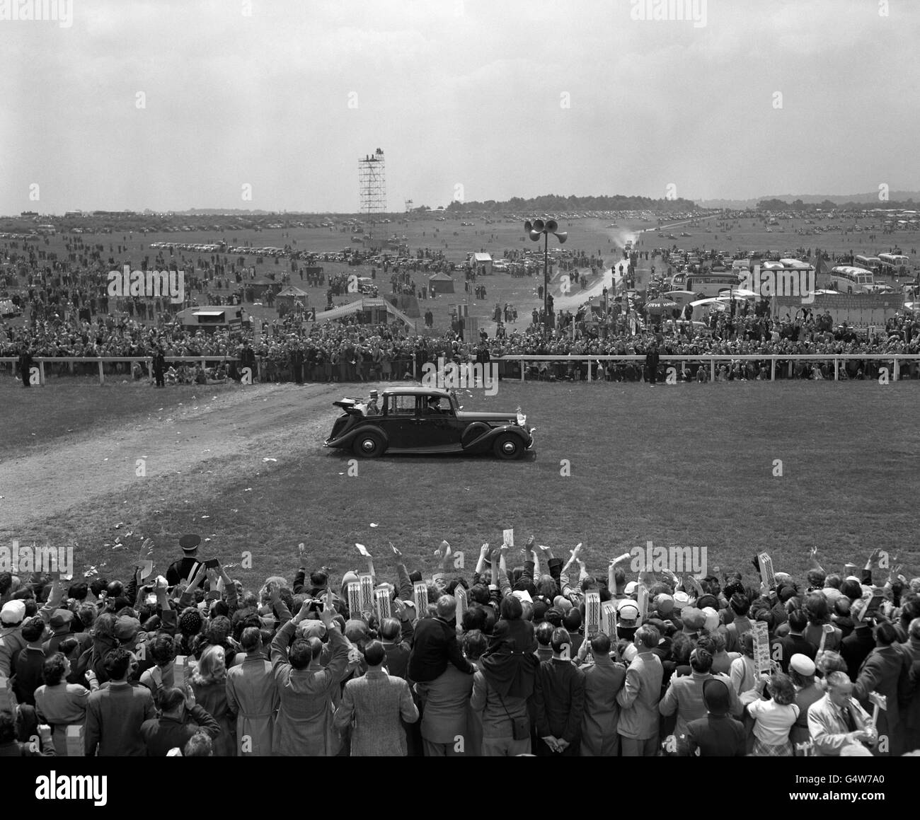 The Queen drives along the course at Epsom in front of the waving and cheering crowd Stock Photo