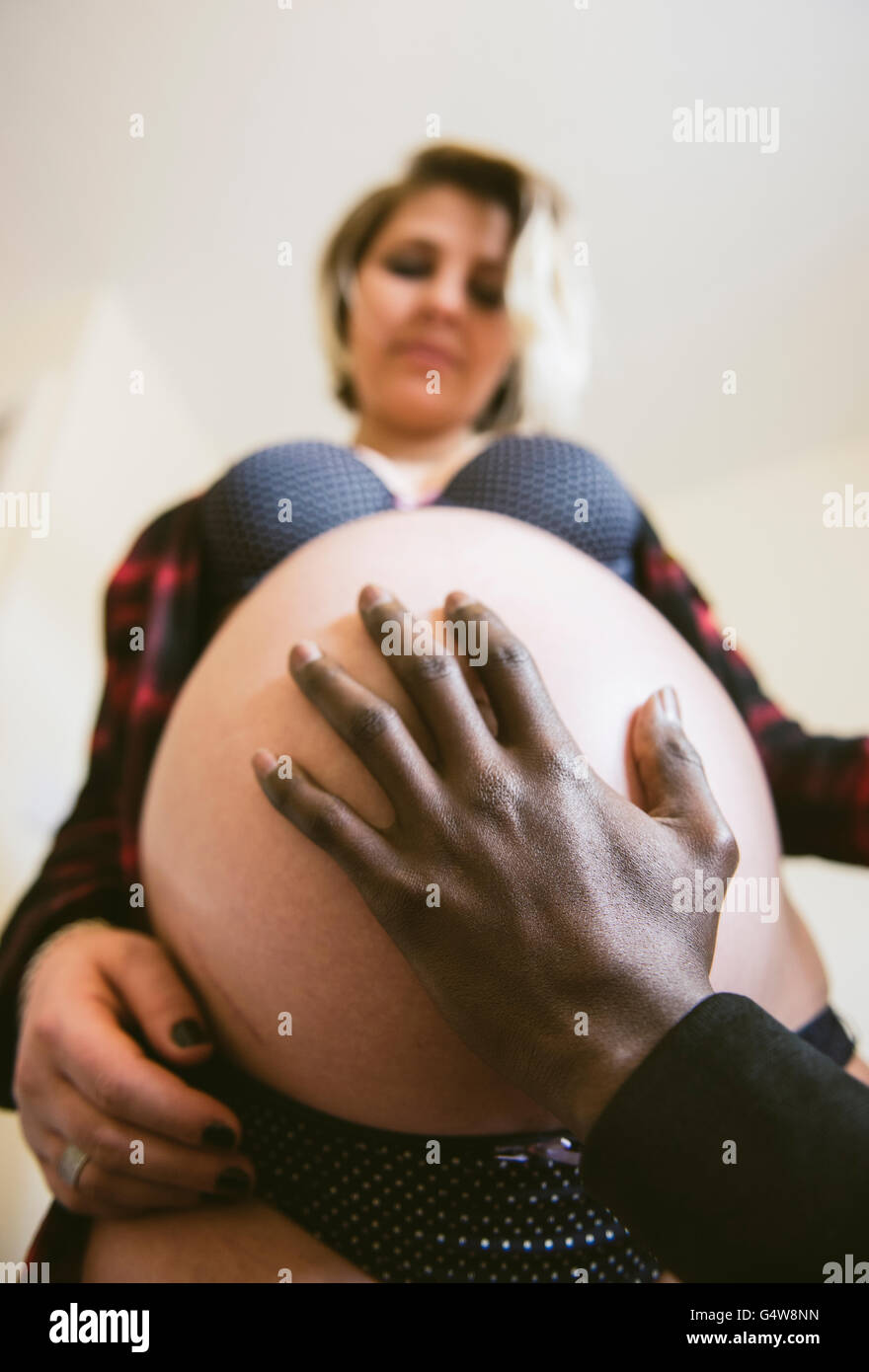 Dad's hand over the baby bump; expectant parents. Stock Photo