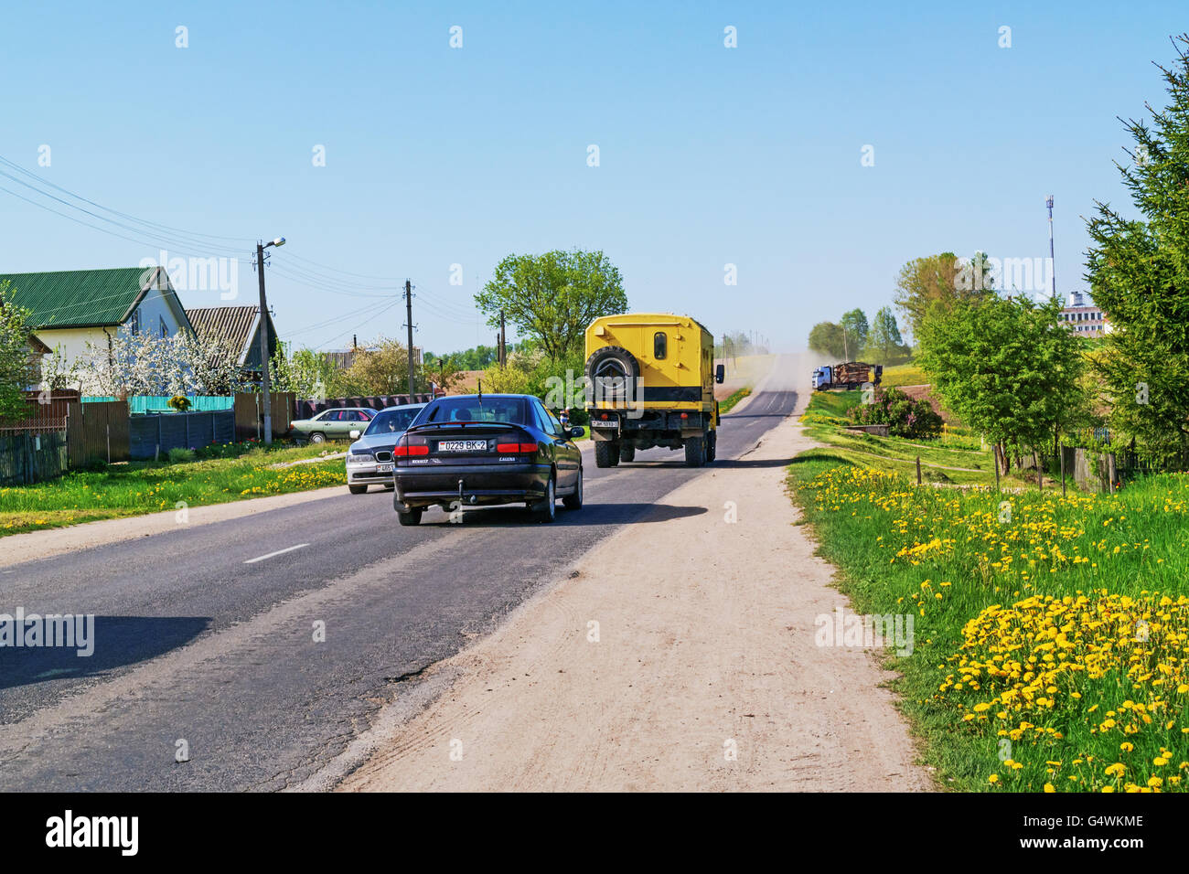 Along the way dandelions grow. on the road going passenger cars and trucks. Stock Photo
