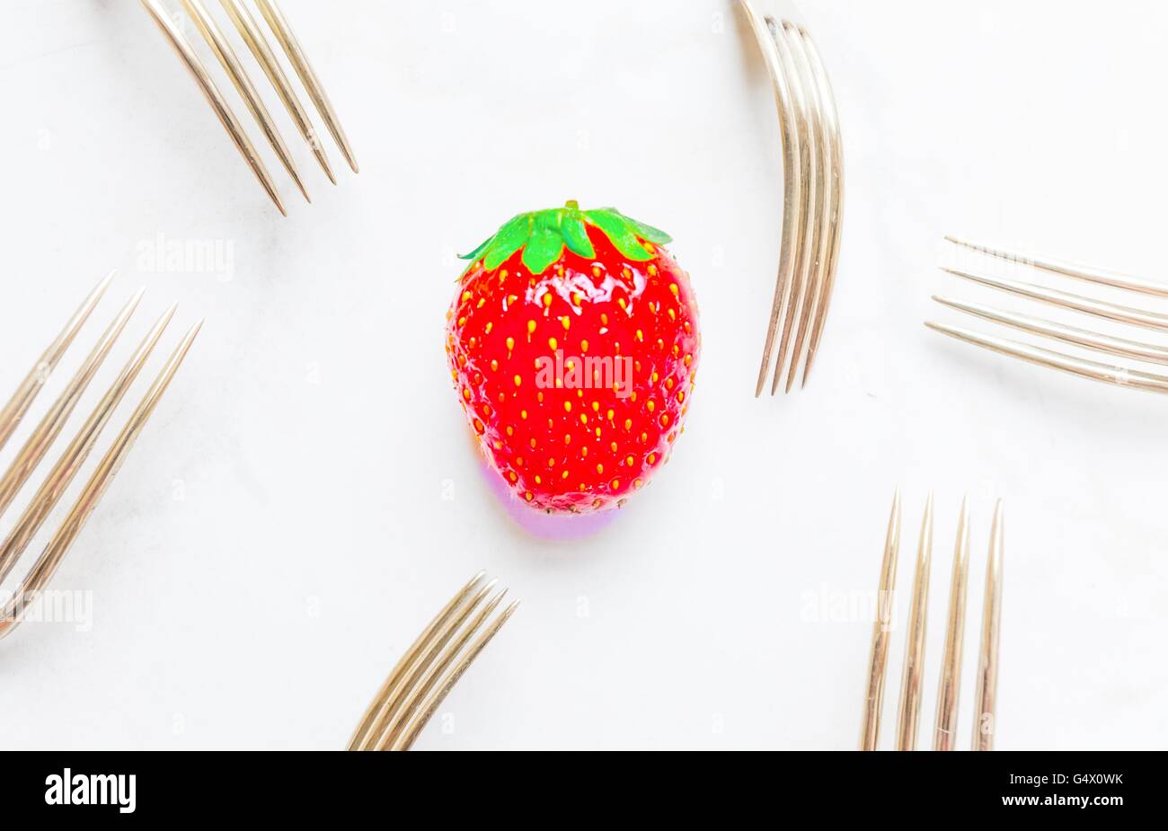 a single strawberry ,over saturated ,surrounded by silver vintage forks Stock Photo