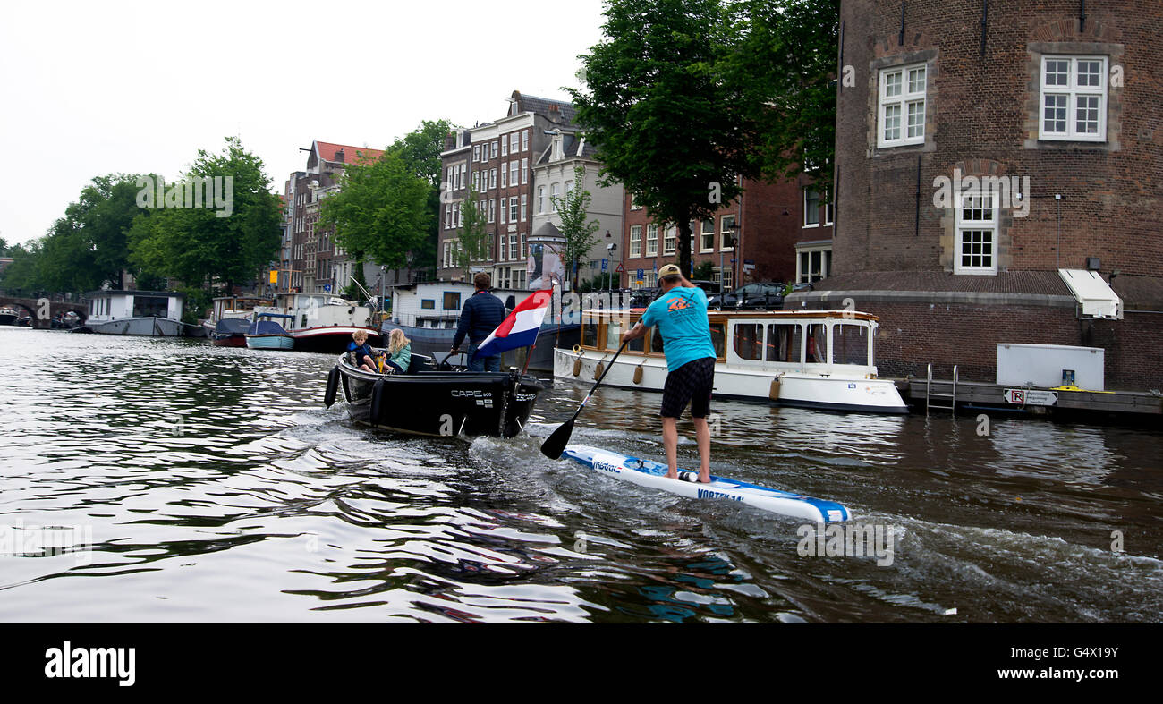 man punts behind a boat along Amsterdam canal. Stock Photo