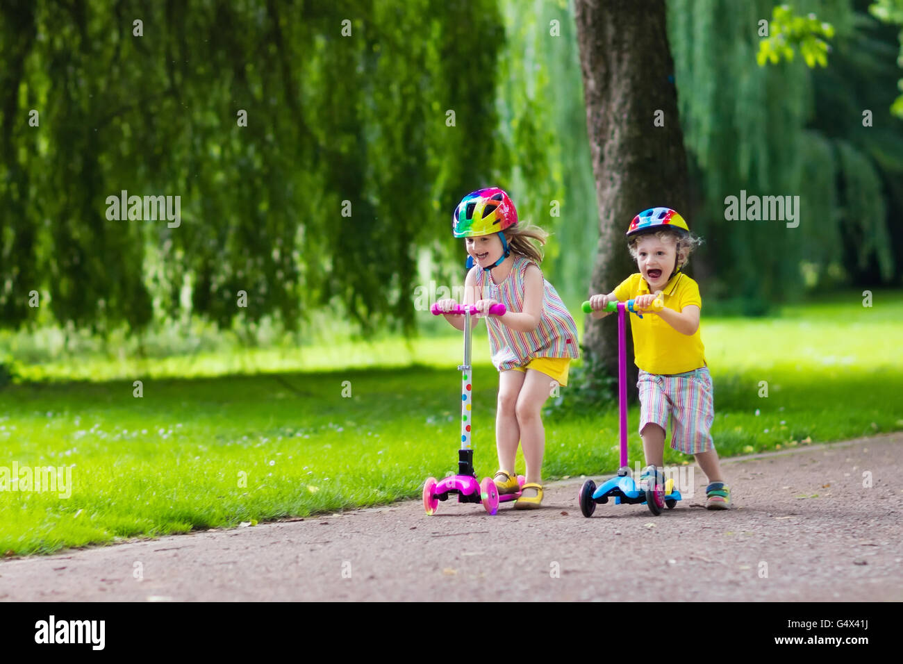 Children learn to ride scooter in a park on sunny summer day