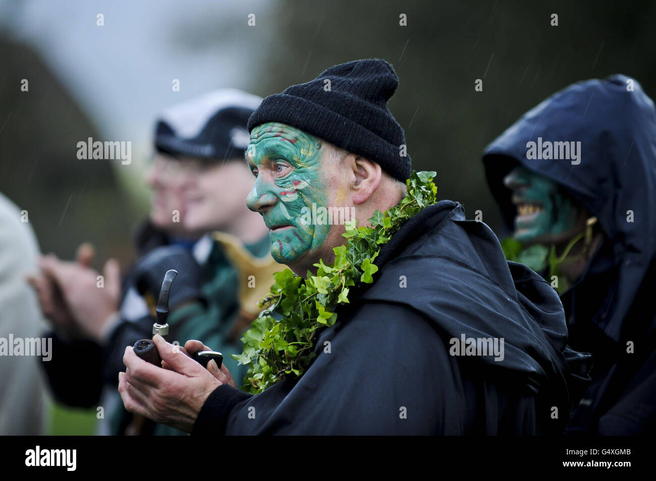 People with painted faces look on as dancers weave around the maypole ...