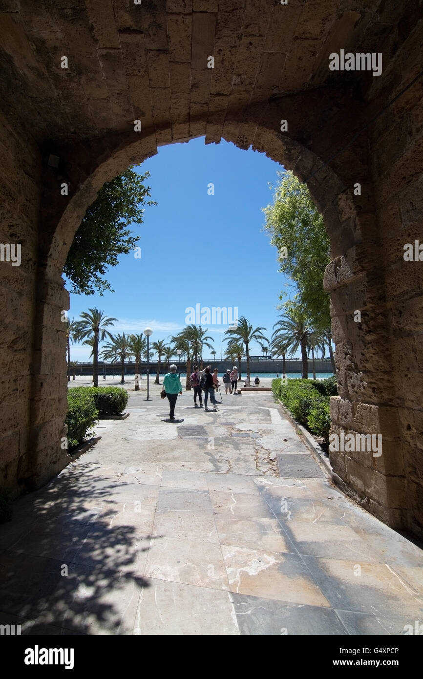 Tourists through portal with a view towards water and palm trees on Passeig Dalt Murada in Palma de Mallorca, Spain. Stock Photo