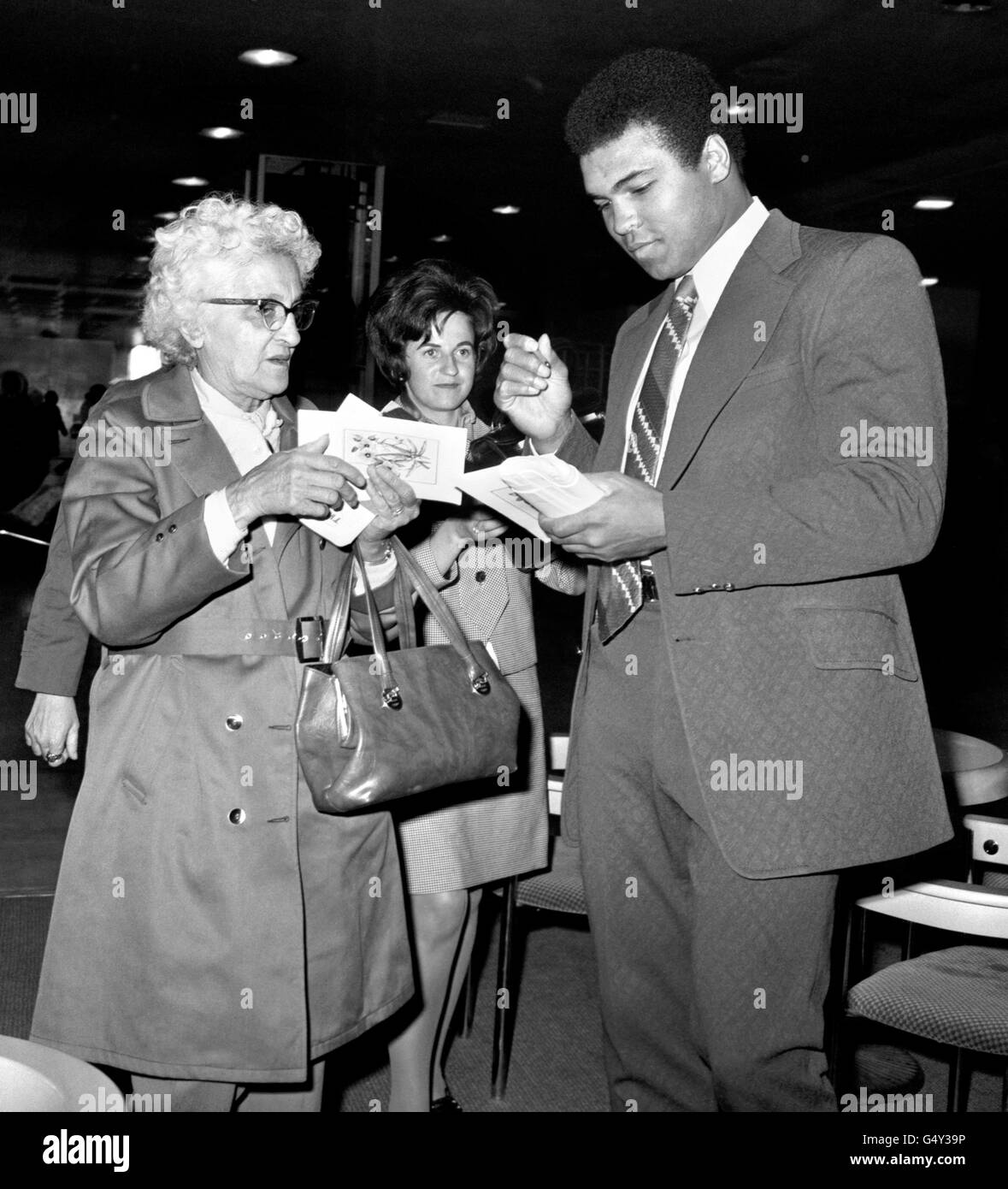 American boxer, Muhammad Ali gives autographs to female fans at Heathrow Airport, before flying out to Saudi Arabia, for a Muslim pilgrimage to Mecca where he plans to celebrate Omra. Stock Photo