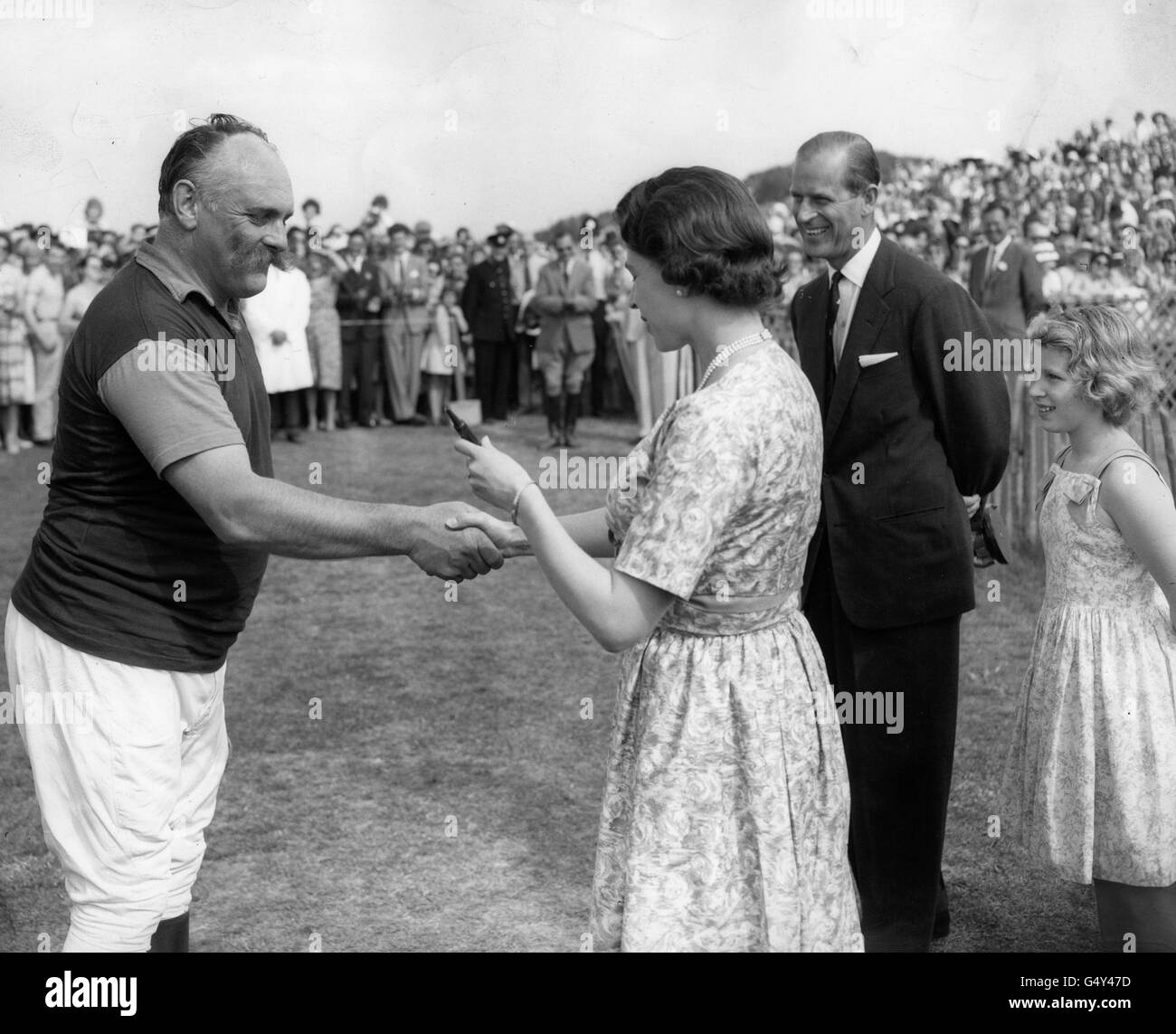 **Low-res scanned off print** Queen Elizabeth II presents a three coloured pencil to comedian Jimmy Edwards, as a consolation prize after his team, Ambersham, has been defeated by Jersey Lillies at polo on Smith's Lawn, Windsor Great Park. The Duke of Edinburgh and Princess Anne look on in amusement. Stock Photo