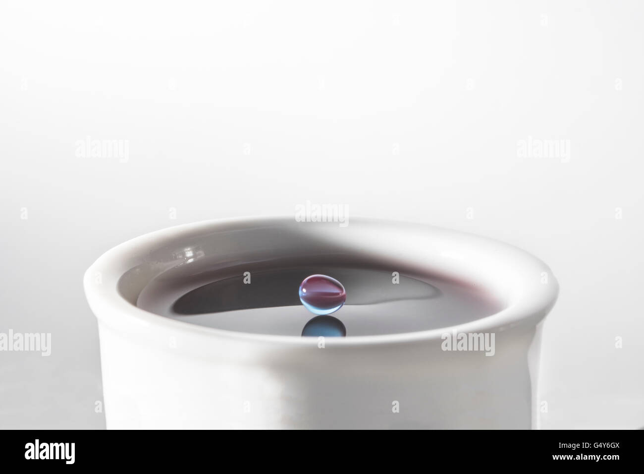 Colored water droplet balancing just before it splashes in cup of water Stock Photo