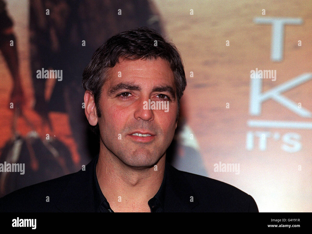 Actor George Clooney poses for the media in front of a poster for his new film, 'Three Kings', in London. Stock Photo
