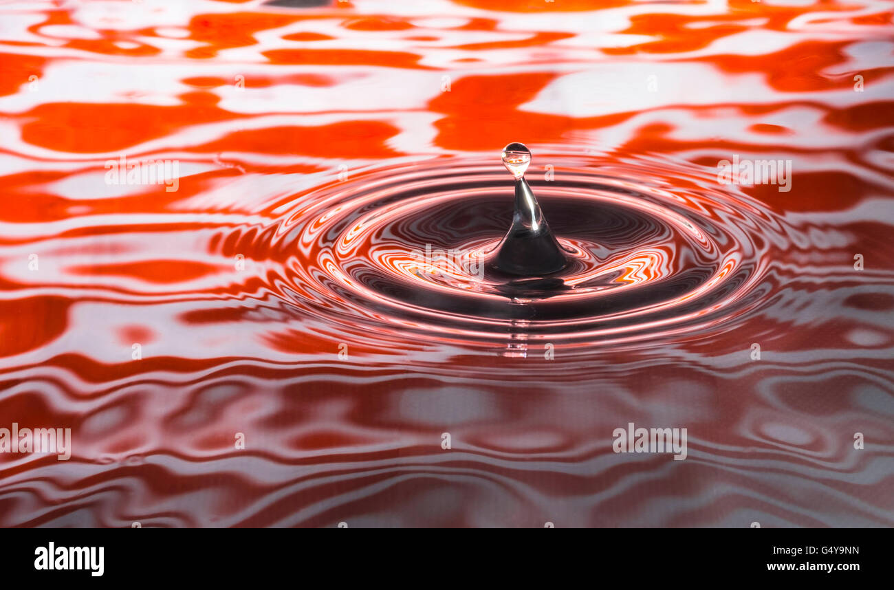 Water drop captured in bright orange colored ripples Stock Photo