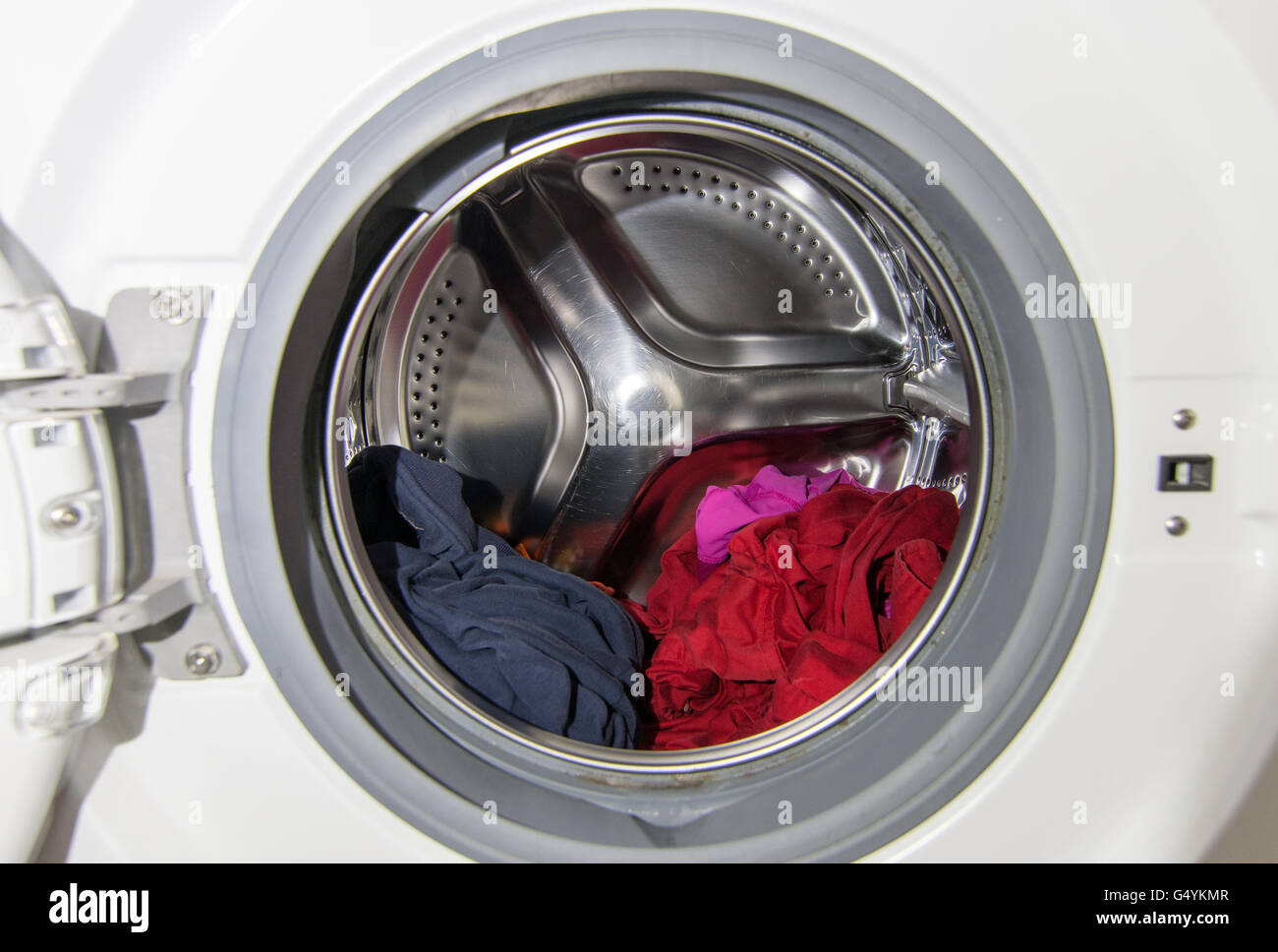 View of the interior of a domestic front loading washing machine with wet laundry inside it. Stock Photo