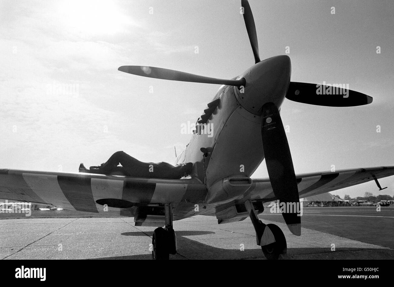Jim Kennedy finds a suitable place to catch the sun on the wing of this vintage Spitfire. The World War Two aircraft is one of many on display at the Biggin Hill International Air Fair Stock Photo
