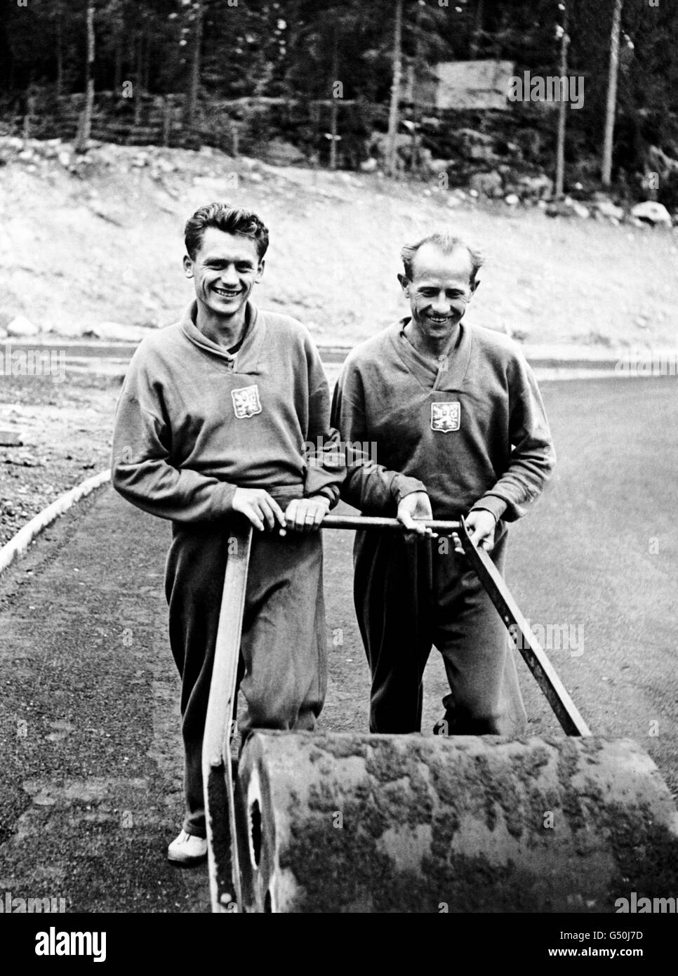 Emil Zatopek, right, the Czech runner, and winner of the 10,000 metres, keeps fit with a turn at the roller, helped by his fellow countryman, Vaclav Cevona, to compete in the 1,500 metres. Stock Photo