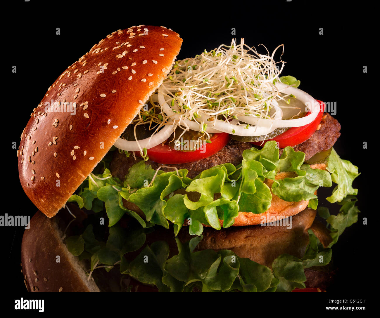 Juicy, tasty burger with pickles, tomatoes, onions and sprouts of flax on a black background Stock Photo
