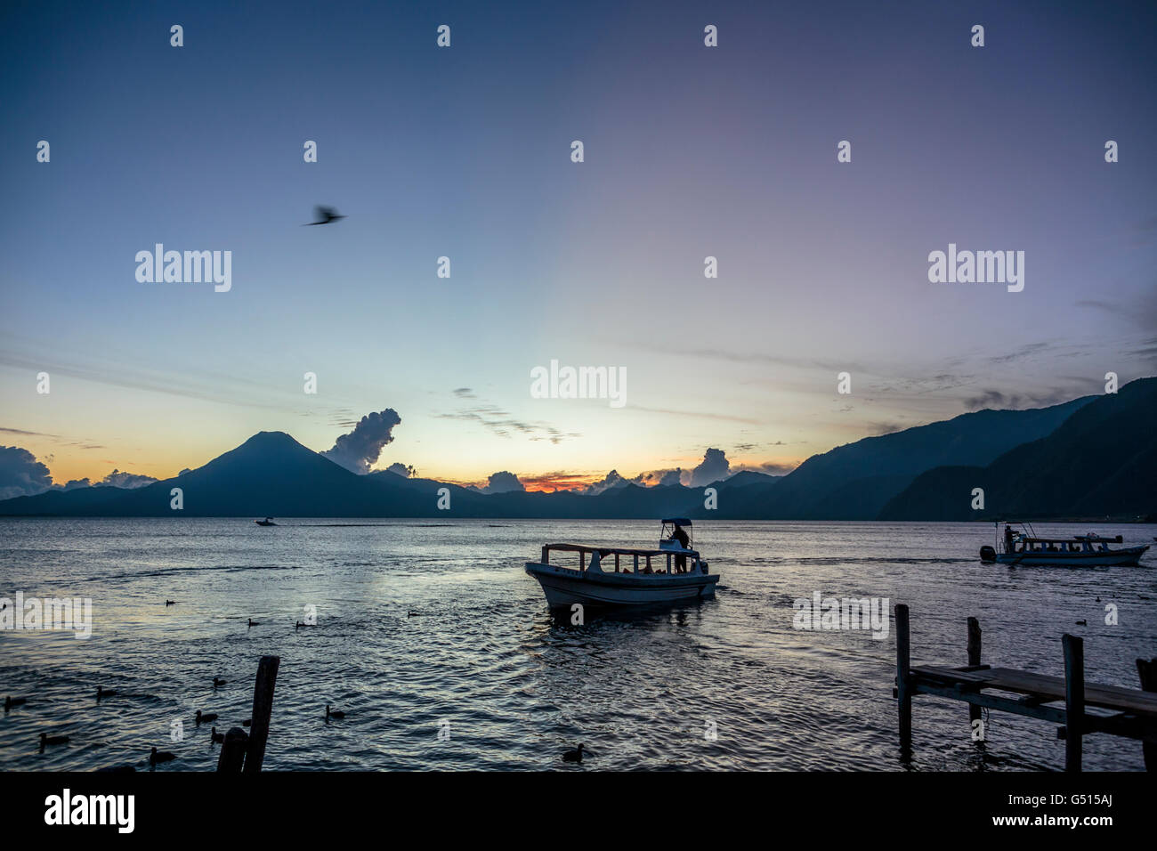 The sun sets over Lago de Atitlan in Guatemala, and the last water taxis bring tourists to the docks in Panajachel at dusk. Stock Photo