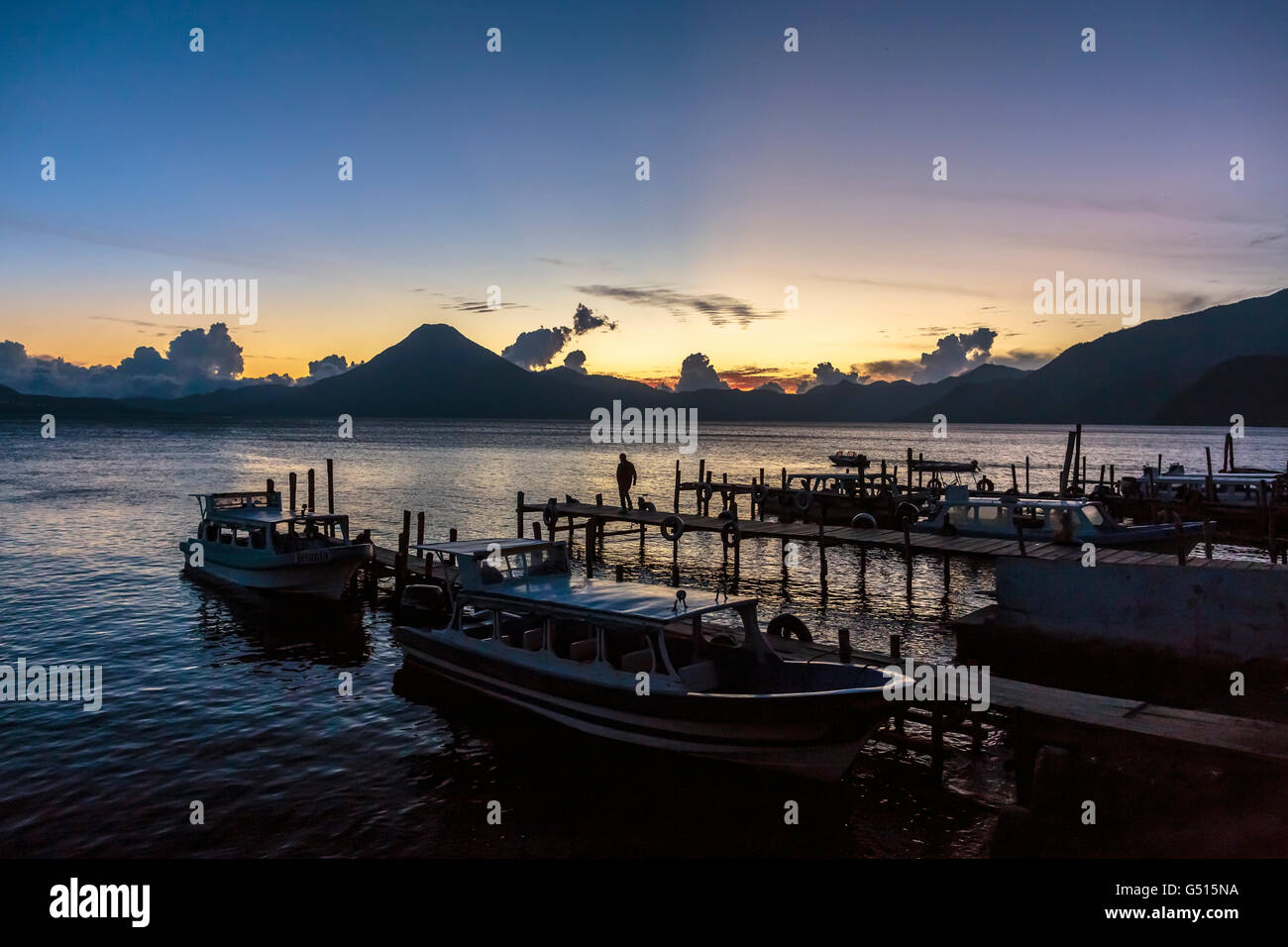 The sun sets over Lago de Atitlan in Guatemala, and tourists and locals gather at the docks in Panajachel to watch dusk settle. Stock Photo