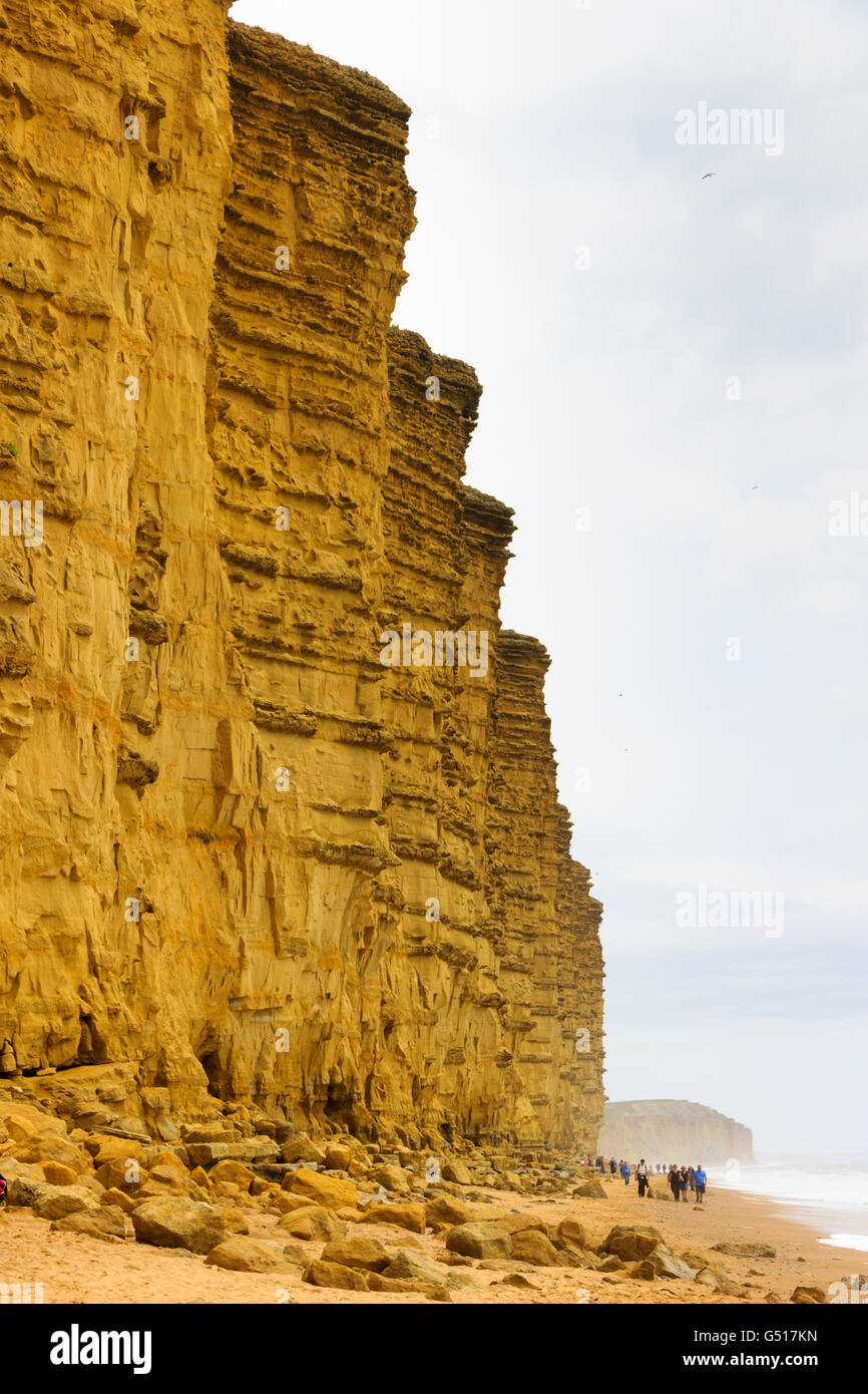 Towering cliffs of Lower Jurassic Bridport Sand formations at West Bay, Dorset, UK, loom over walkers on a misty June day Stock Photo
