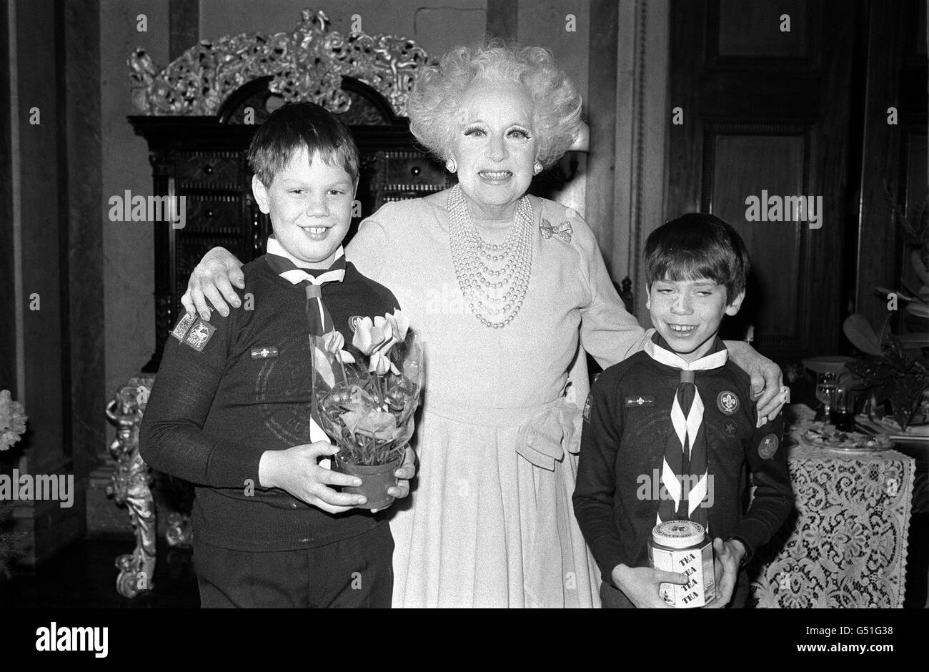 PA Photo 11/12/1984 Barbara Cartland takes tea with two young cub scouts at her Hatfield home Herfordshire, part of a nationwide 'Take Time for Tea' scheme. BBC Television John Craven who is fronting the scheme involving some 500 cub scout packs looks on as Simon Redman (10 years old right) and Ashley Williams (9 years) serve tea to the authoress Stock Photo