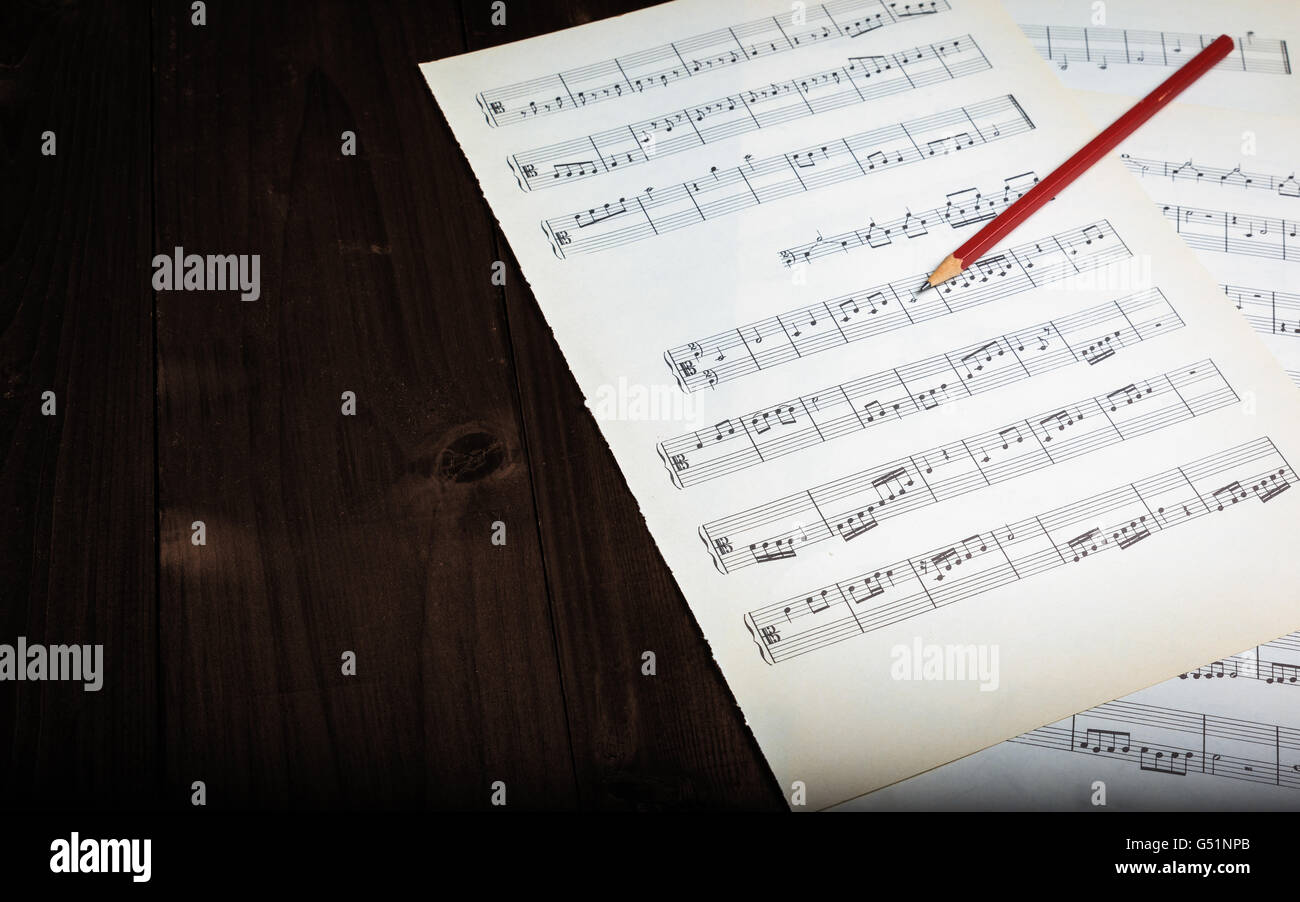 In the picture aged pages of sheet music, pencil  and wooden background. Stock Photo