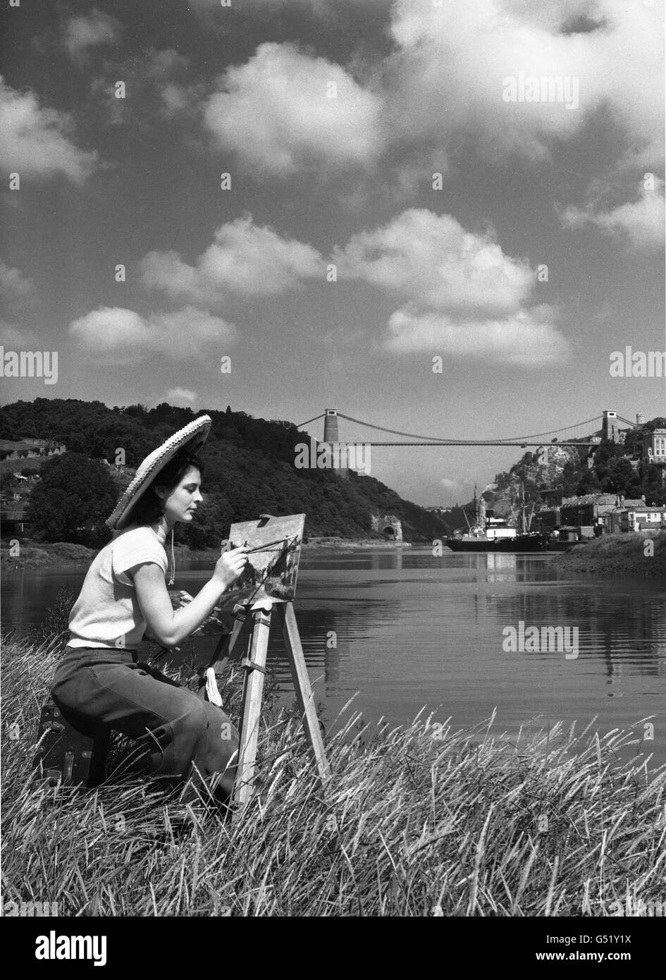 An ideal spot for an artist to record the beauty of rural England is this bank on the River Avon on which Jean Yates, of Bristol, sits to record the tranquillity of cloud, hill and water. Miss Yates is an artist's model and a keen amateur artist herself. In the background is the Clifton Suspension Bridge. Stock Photo