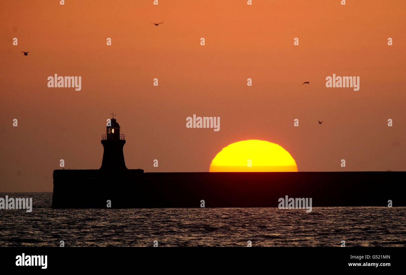 A huge sun rises over the lighthouse in South Shields at the mouth of the Tyne estuary, Tyne and Wear, as Britain looks set to bask in sunshine this weekend with temperatures topping those of many European destinations. Stock Photo