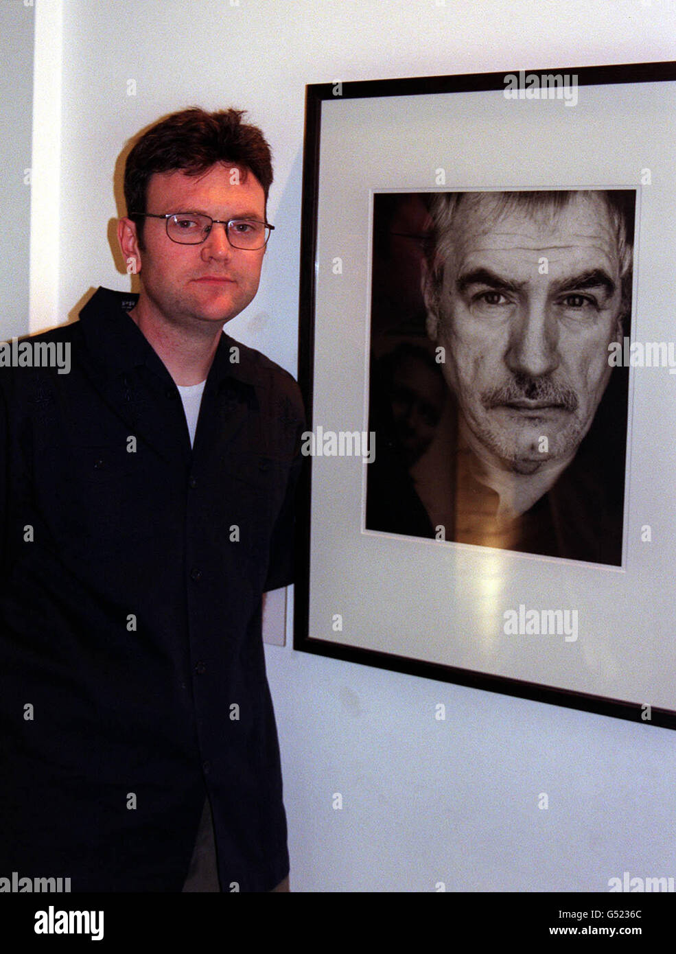 Photographer Donald Maclellan in front of his portrait of actor Brian Cox at an exhibition of his photography at the National Portrait Gallery in London. * The new exhibition of 22 photographic portraits by MacLellan celebrates the growing prominance of Scottish actors in contemporary cinema. Included in the exhibition, opened by TV presenter Gail Porter are Ewan MacGregor, Kelly MacDonald and Robert Carlyle who rose to fame in Danny Boyle's 'Trainspotting'. PA photo: Maev Allen. Stock Photo