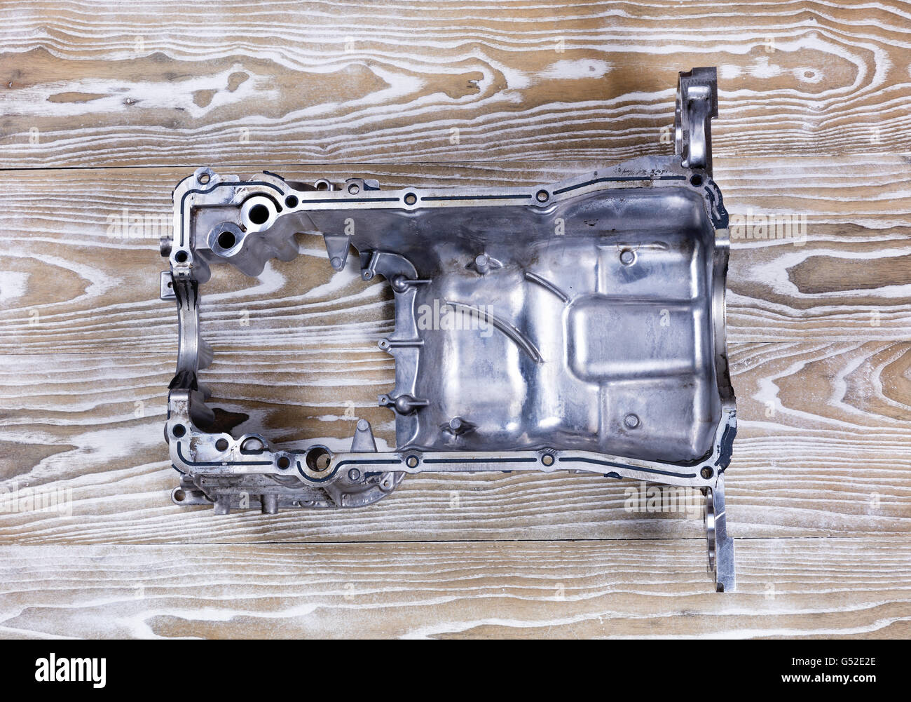 Overhead view of the inside of a defected aluminum car engine oil pan on rustic white boards. Stock Photo