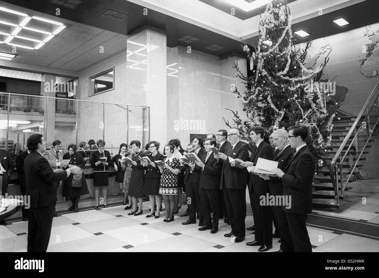 Extra interest for the customers at the Old Broad Street branch of Barclays Bank International in the city when carols were sung by a choir from members of the banks operatic and msuical societies. Stock Photo