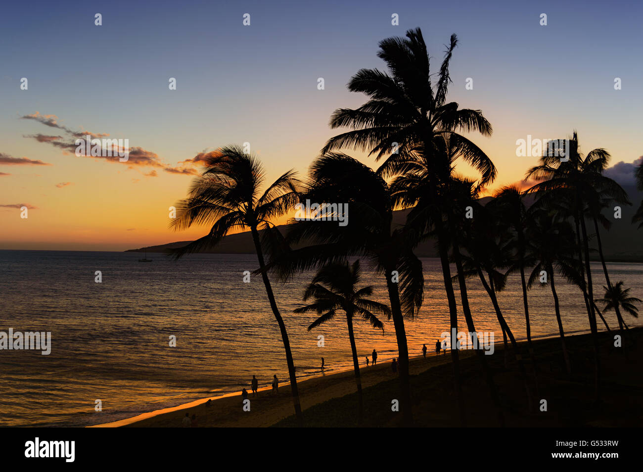 Palm trees and the ocean against a beautiful Maui sunset with people walking on the beach Stock Photo