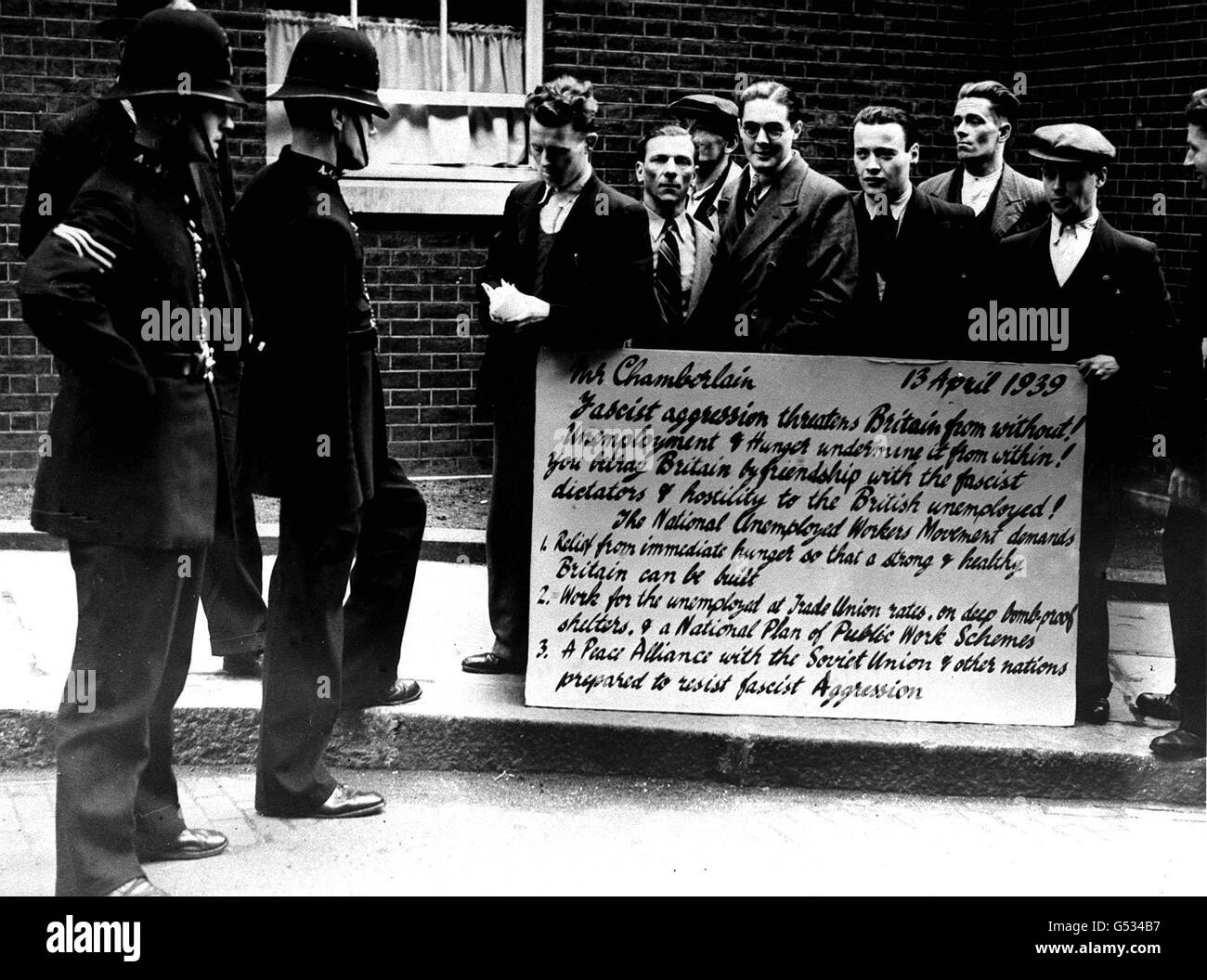 1930s UNEMPLOYED: A group of men from the National Unemployed Workers Movement in Downing Street, London, with a 'protest postcard' listing various grievances and suggestions for the attention of the Prime Minister, Neville Chamberlain. Stock Photo