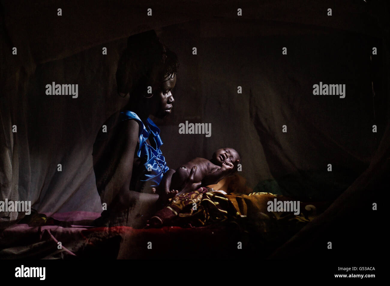 A woman holds her new born baby inside her mosquito net after she gave birth in the Goal clinic in Balliet,a village along the Sobat River in the Greater Upper Nile region of northeastern South Sudan, Africa.The region recently suffered from serious inter tribal fighting resulting in thousands of people forced into internally displaced people (IDP) camps.Goal ,the Irish aid agency working in Sudan since 1985 has been at the forefront of providing aid and shelter to Sudanese people affected by war and poverty. Stock Photo