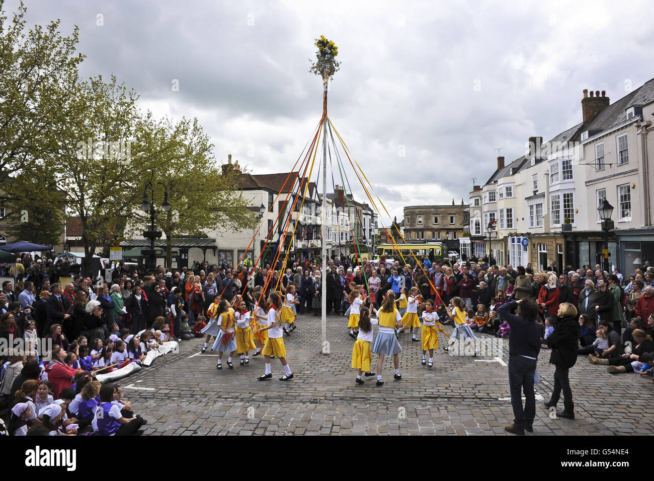 PHOTO. Girls from St. Joseph and St. Teresa schools perform Maypole dances in Wells Market Place on Mayday bank holiday Monday, a tradition where people used to cut down young trees and stick them in the ground in the village to mark the arrival of summer. People then danced around the tree poles in celebration of the end of winter and the start of the fine weather, which would allow planting to begin. Stock Photo