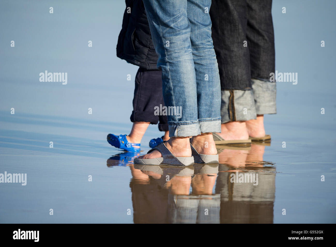 detail close up of adults and child's sandals and feet standing on wet