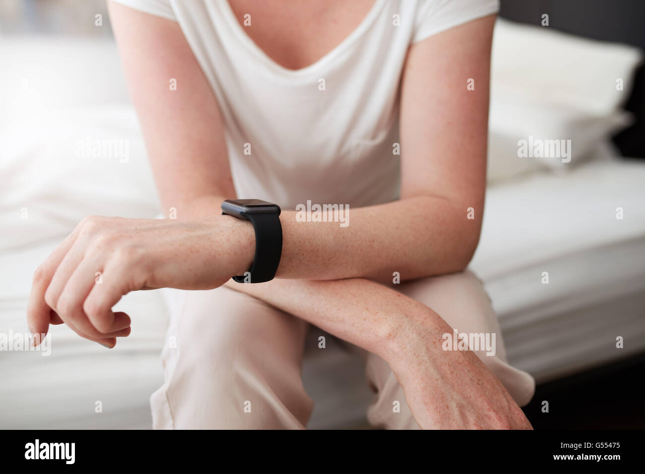 Cropped shot of a woman sitting on bed wearing a wrist watch, she is in bedroom at home. Focus on female hands and wrist watch. Stock Photo