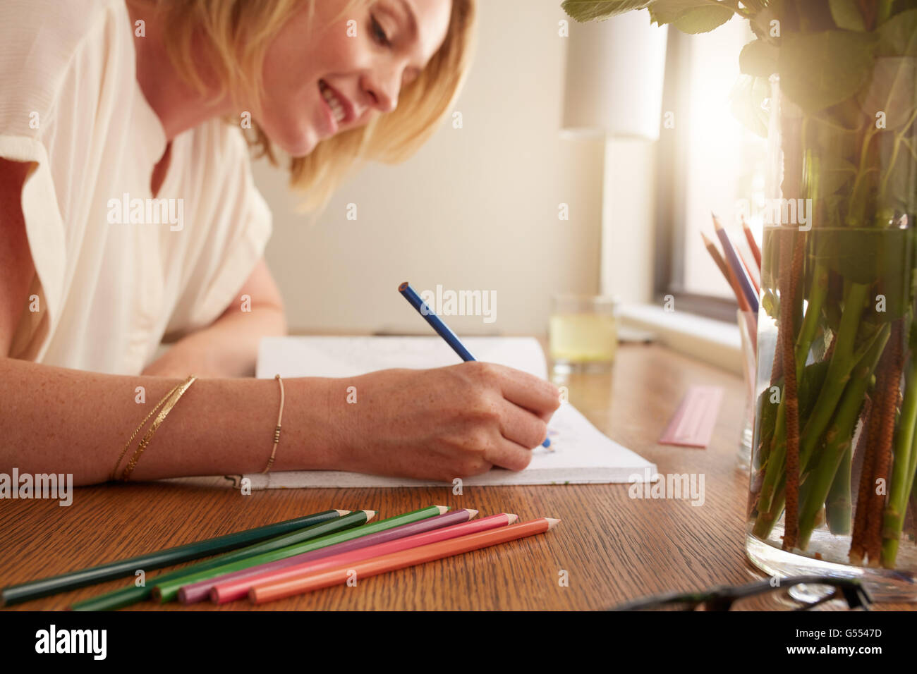 Close up of relaxed woman coloring an adult coloring book with pencils, she is sitting on a table at home. Stock Photo