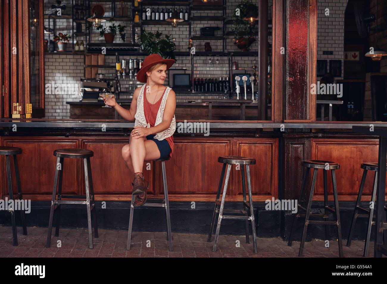 Portrait of stylish young female sitting at a cafe with drink and looking away. Beautiful caucasian female at coffee shop counte Stock Photo