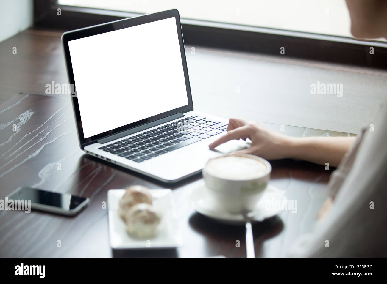 Female hands on laptop touch pad. Woman sitting with cup of coffee and cakes and surfing the internet. Attractive model Stock Photo