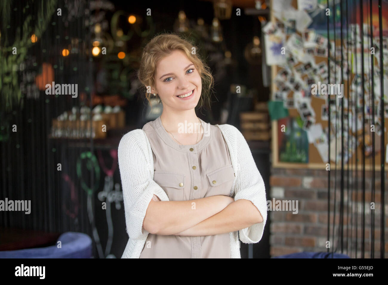 Half-length portrait of young beautiful female standing at her work place with crossed arms. Woman welcoming customers Stock Photo