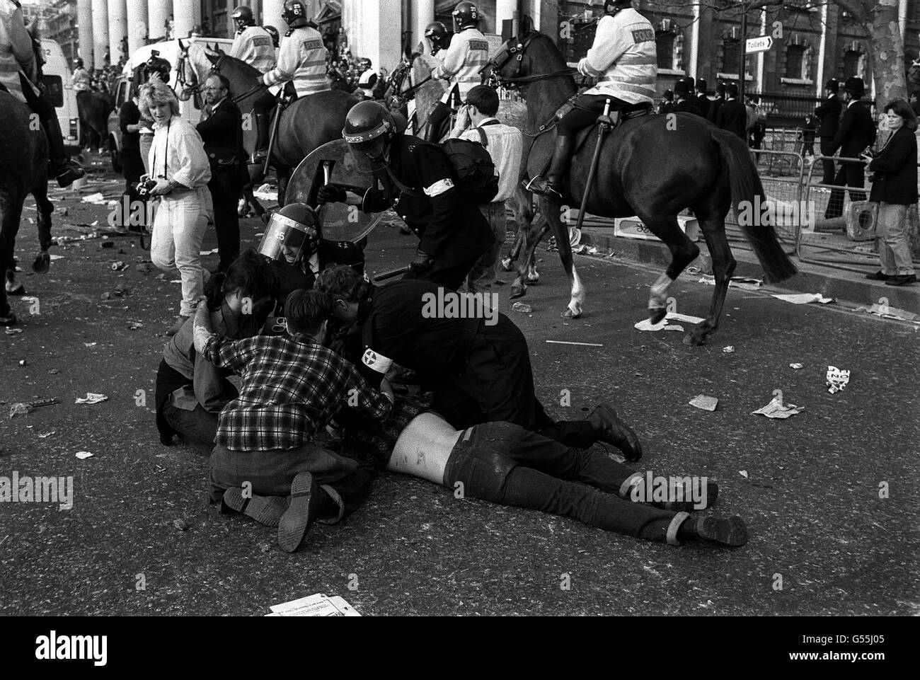 Police officers attend to an injured man in Trafalgar Square, London, after an anti-poll tax demonstration degenerated into a riot. Mounted police officers can be seen heading in the direction of Charing Cross Rd. Stock Photo