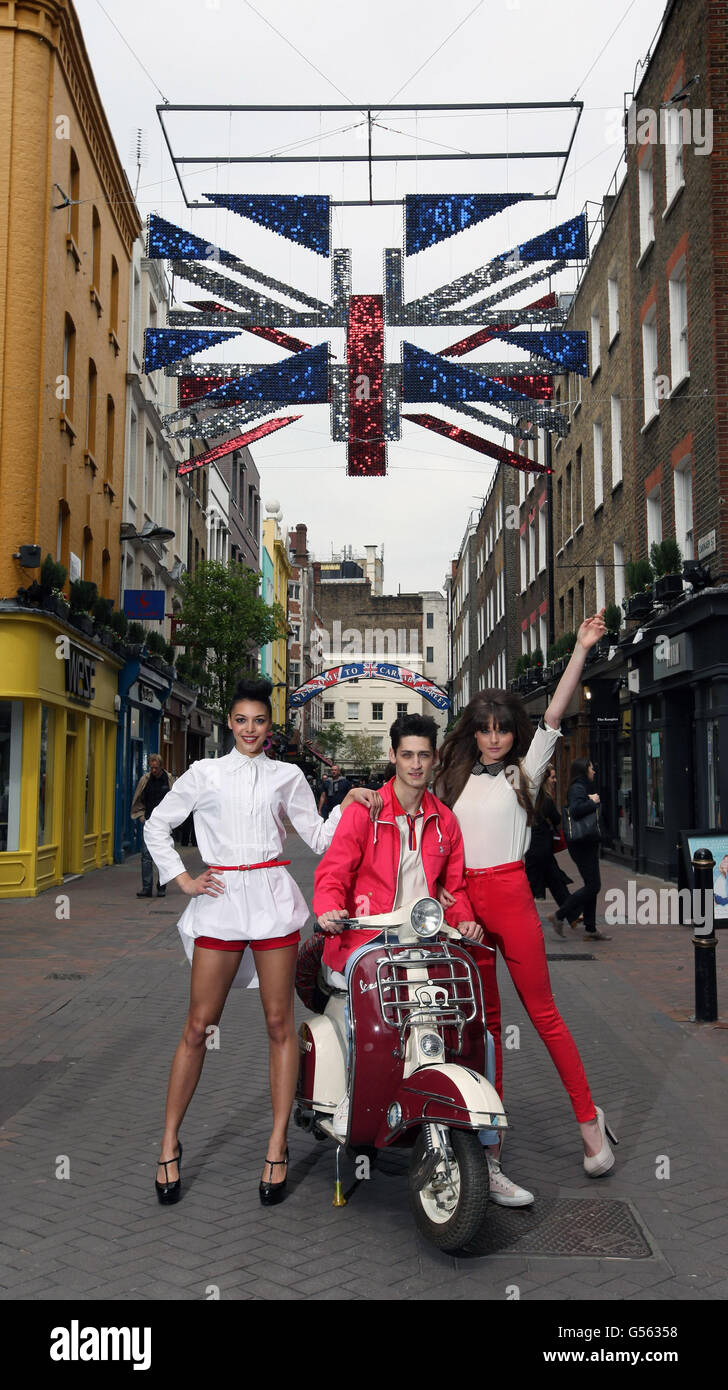 Models Carlos, Mecia and Jodie stand beneath a deconstructed 3 dimensional Union flag covered in thousands of metallic red, white and blue shimmer discs is suspended above Carnaby Street in central London as part of the oversized public art installations for the Diamond Jubilee. Stock Photo