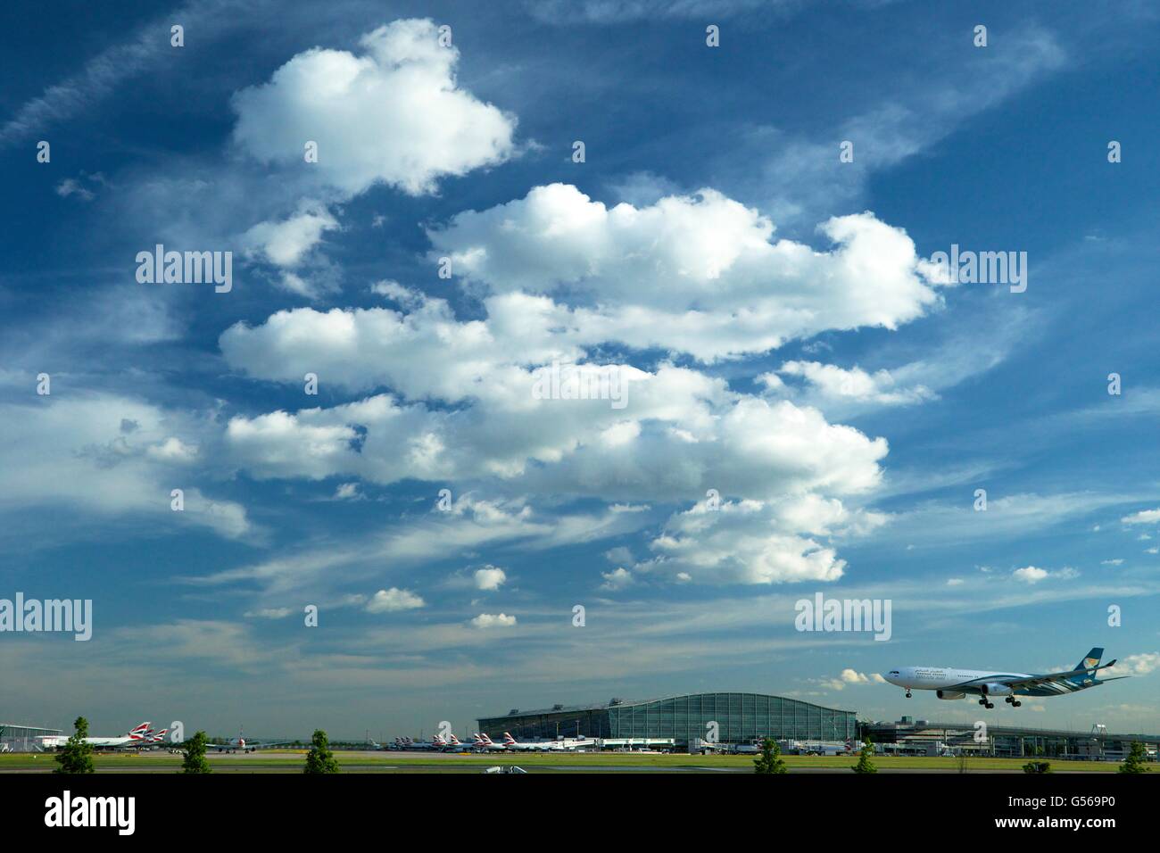 Oman Air flight landing at Heathrow Airport with Terminal 5 behind, London, England, UK, GB, Stock Photo