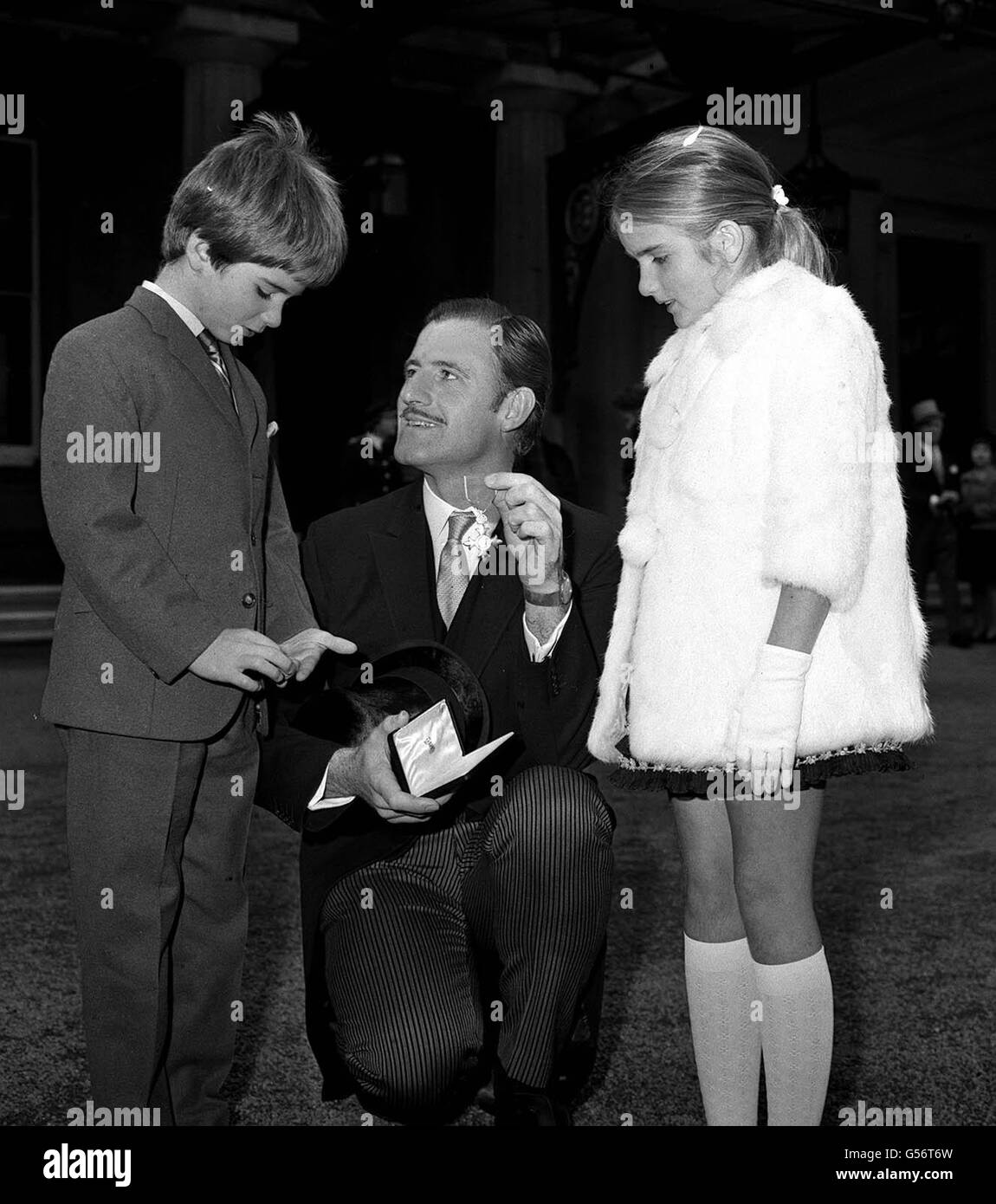 GRAHAM HILL 1968: Racing driver Graham Hill showing his children Damon (8), left, and Brigitte (9), the OBE he received from the Queen Mother at his investiture at Buckingham Palace, London. The Queen Mother congratulated him on his second world championship and asked about his victory in the Mexican Grand Prix. Stock Photo
