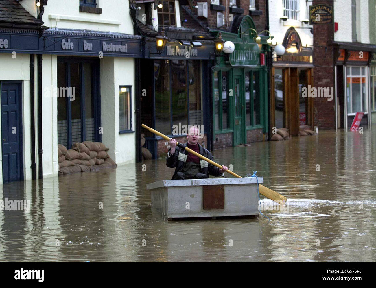 A man in a boat struggles through flood water in central Shrewsbury. The Peach Tree Restaurant, seen left, was flooded again for the third time in six weeks. The restaurant owner, Martin Monahan, has vowed that it will be business as usual despite the flooding. *15/06/04: Two billion people worldwide will be at risk of devastating flooding by 2050 due to climate change, deforestation and rising sea levels, according to a warning issued by experts at the United Nations University. One billion people are estimated to live in the potential path of a 100-year flood. Stock Photo