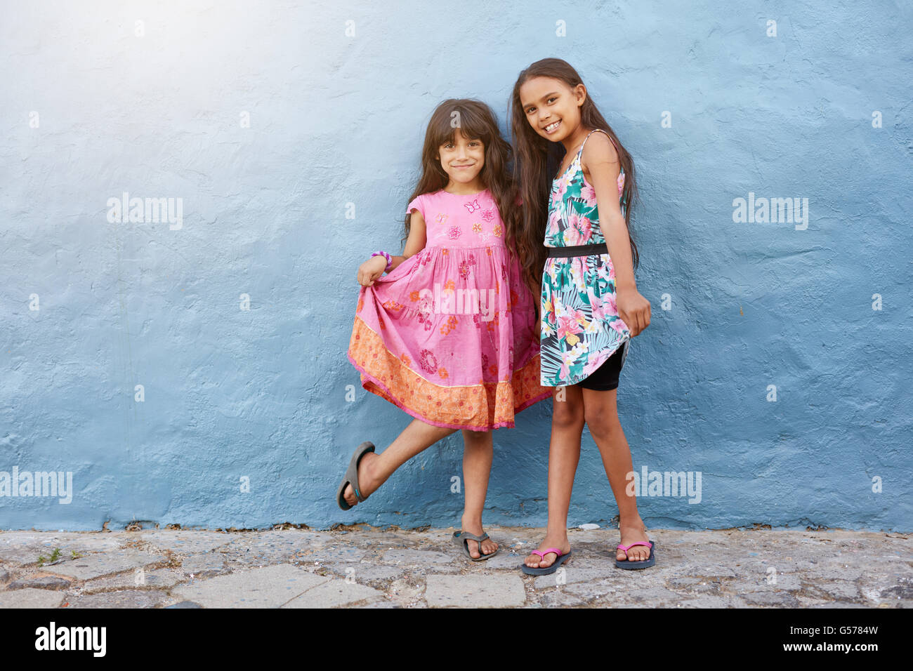 Full length portrait of two happy little girls standing by a blue wall. Girls wearing beautiful dress posing to the camera with Stock Photo