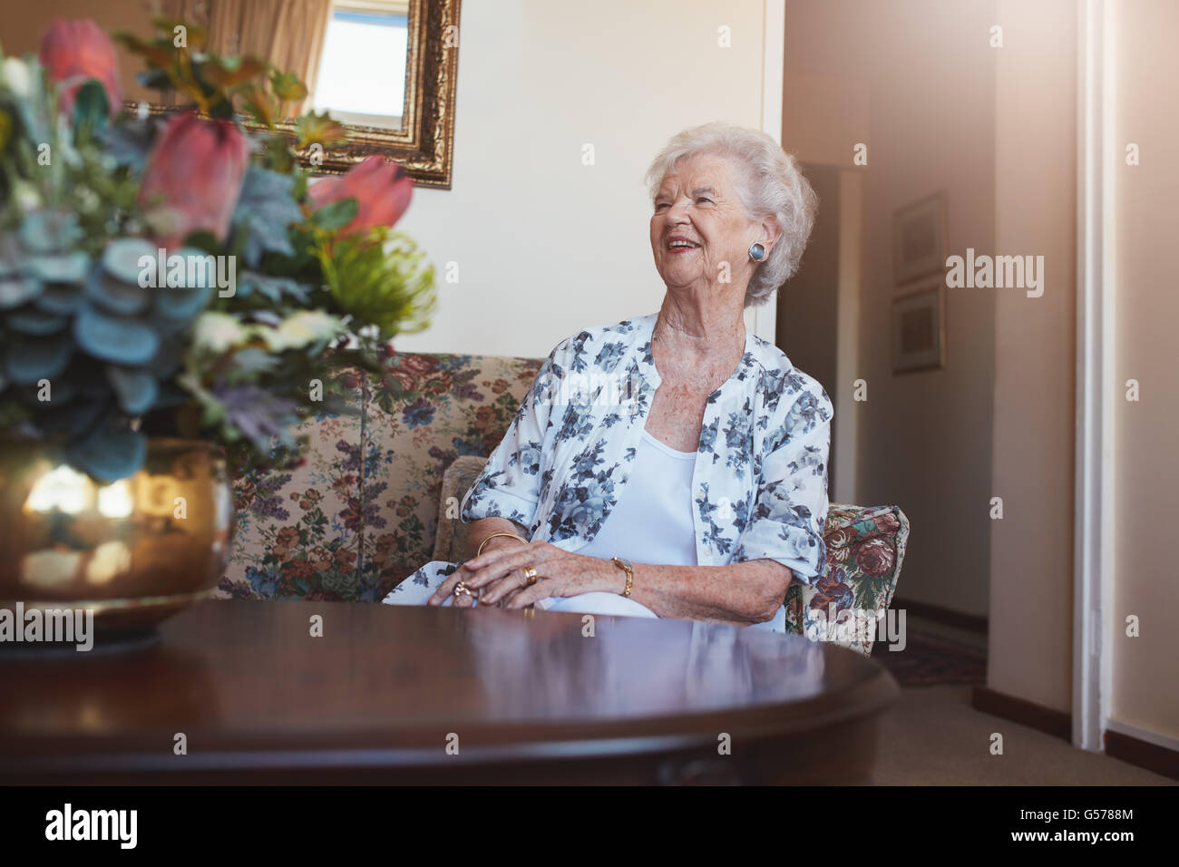 Portrait of a senior woman sitting on a sofa at old age home looking away and smiling. Stock Photo
