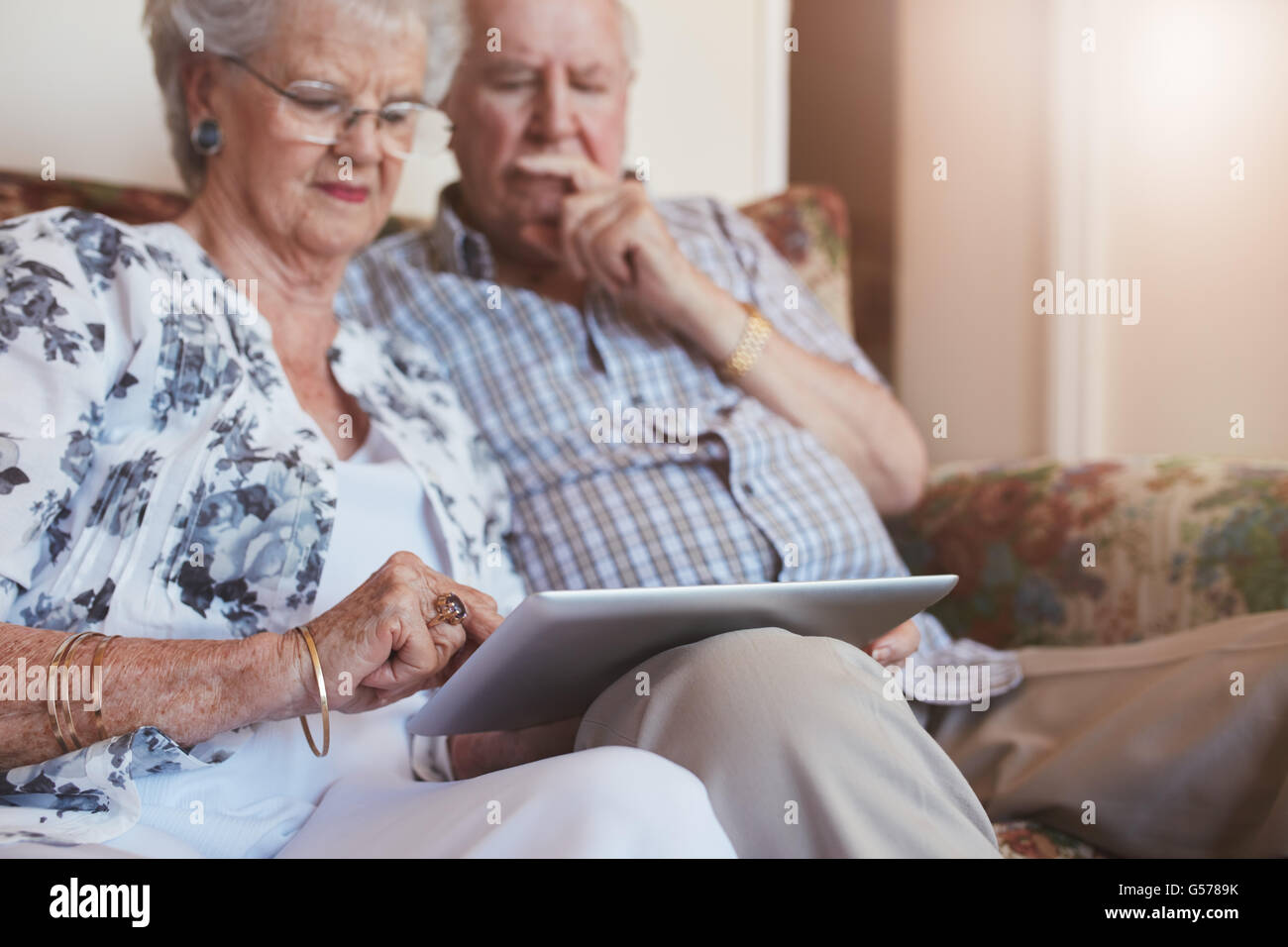 Portrait of elderly woman sitting with her husband and using digital tablet. Retired couple sitting on sofa at home with a touch Stock Photo