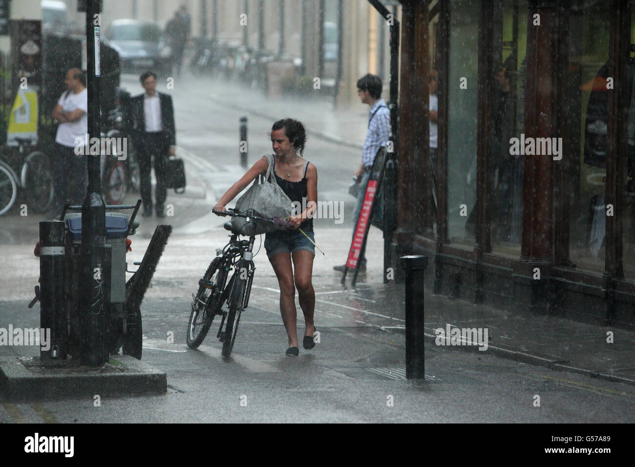 A young woman walks with her bike after being caught in a thunder storm in Oxford city centre. Stock Photo